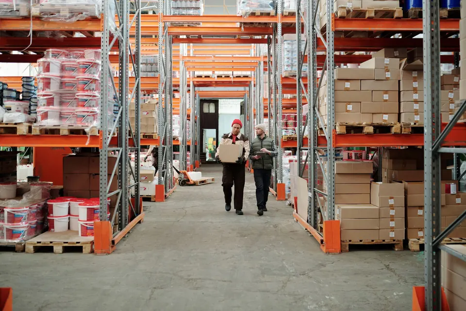 Warehouse team handling a parcel between stocked shelves